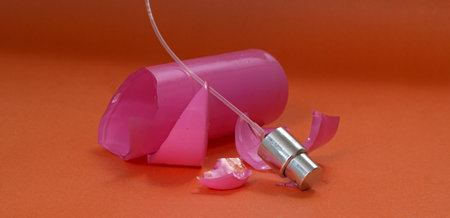 Broken pink perfume bottle on orange background.