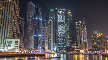 Dubai marina bay with yachts an boats timelapse. Tallest skyscrapers illuminated by night reflected in water of canalの写真素材