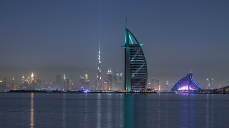 Skyline of Dubai by night with Burj Al Arab from the Palm Jumeirah timelapse. Illuminated skyscrapers reflected in waterのeditorial素材
