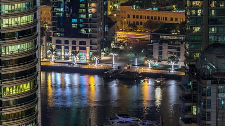 Beautiful aerial top view at night timelapse of Dubai Marina promenade and canal with floating yachts and boats in Dubai, UAE. Illuminated modern towers with blinking lights and traffic on the road.の写真素材