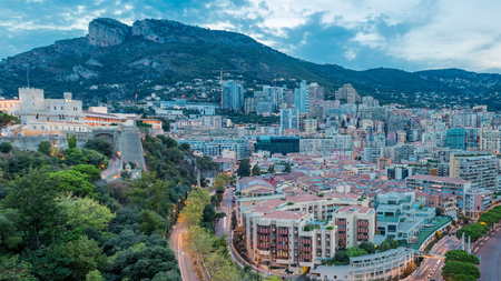 Panorama of Monte Carlo day to night transition timelapse from the observation deck in the village of Monaco near Port Hercules. Buildings with illumination and hills on background aerial top view. Traffic on the roadの写真素材