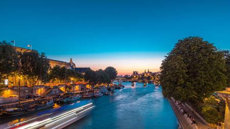 View on Pont des Arts in Paris after sunset day to night transition timelapse from Pont Neuf, France. Ship on the River Seine near square of the Vert-Galant. Reflection on waterの写真素材