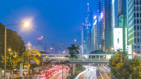 Hong Kong street with busy traffic and skyscraper office at dusk day to night transition timelapse. Lights turning on. View from bridge in central part. 4Kの写真素材