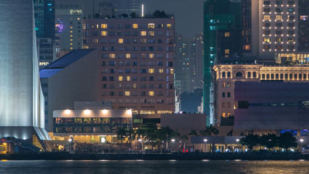 People sitting on the stairs near Hong Kong Cultural Centre with palms and towers on background...