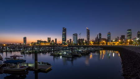 Yachts and boats at the Sharq Marina with city skyline night to day transition timelapse in Kuwait. Kuwait City, Middle East. Modern towers reflectied in the waterの写真素材