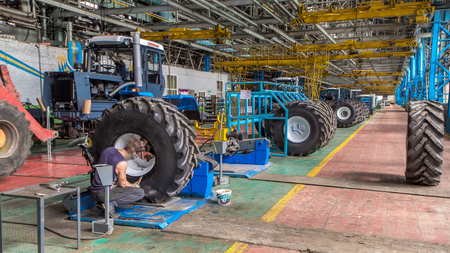 Professional mechanic install big tires on tractor wheels in repair service on tractor factory...