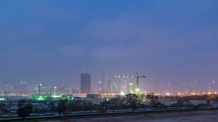 Skyline of construction cranes tower with skyscrapers on background in the Middle East day to night transition timelapse, Dubai. Evening mist. Cloudy skyの写真素材
