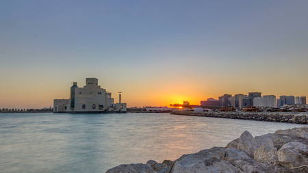 Doha Harbor with passing fishing boats during sunrise timelapse with museum of islamic art on background. Doha, Qatar, Middle-East. Stones on foreground.の写真素材