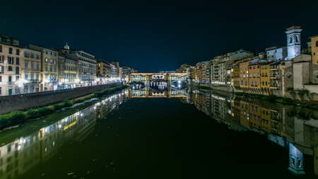 Famous Ponte Vecchio bridge timelapse over the Arno river in Florence, Italy, lit up at night. Reflection on water. Old houses on the sideの写真素材
