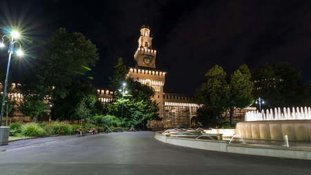 Main entrance to the Sforza Castle and tower - Castello Sforzesco illuminated at nigh timelapse hyperlapse, Milan, Italy. Fountain and people walking aroundのeditorial素材