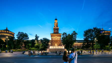 Main entrance to the Sforza Castle and tower - Castello Sforzesco illuminated day to nigh transition timelapse, Milan, Italy. Fountain and people walking aroundのeditorial素材