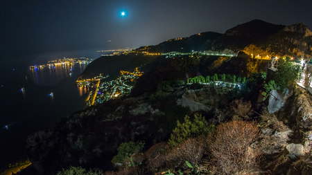 Night timelapse view of the Mediterranean coastline with moon and medieval houses with illumination from the top of the town of Eze village on the French Riviera.の写真素材