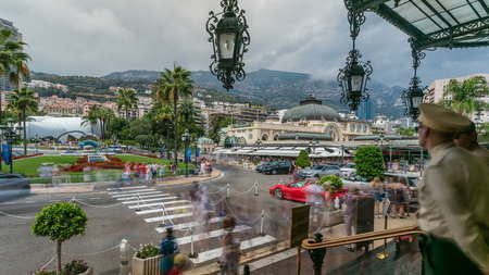 Tourists make pictures near expensive cars and famous Casino building timelapse in Monte Carlo in Monaco. View from stairs of casino main entrance. Square with palms on backgroundの写真素材