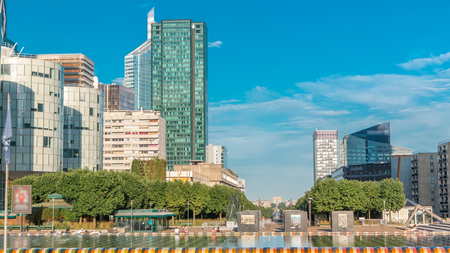 Skyscrapers of La Defense with fountain timelapse - Modern business and residential area in the near suburbs of Paris, France. Arc de Triomphe with Champs Elysees on background. Green trees, blue cloudy sky at sunny summer dayの写真素材