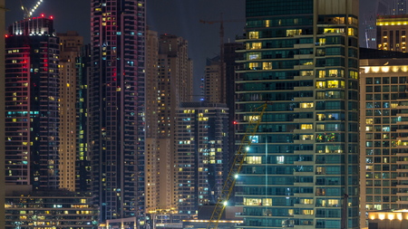 Aerial view of Dubai Marina from a vantage point night timelapse. Modern skyscrapers and residential towers illuminated with glowing windows. Traffic on the roadの写真素材