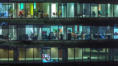 Working evening in glass office building with numerous offices with glass walls and illuminated...