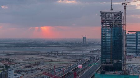 Sunrise aerial view of Financial center road morning timelapse with intersection and under construction building with cranes from downtown, Dubai Creek harbor on backgroundの写真素材