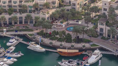 Aerial view on yachts floating in Dubai marina timelapse. White boats are in green canal water. Promenade with shops and restaurants.の写真素材