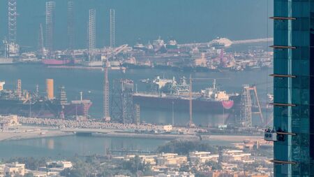 Aerial morning view from Downtown of Dubai timelapse with windows cleaners on skyscraper, houses and port Rashid on a background, ships docking at sea port, UAEの写真素材
