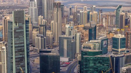 Panoramic aerial view of business bay towers and downtown in Dubai at evening timelapse. Rooftop view of some skyscrapers, canal and new towers under construction.の写真素材