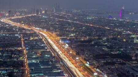 Aerial view to traffic on Sheikh Zayed road and intersection day to night transition timelapse, Dubai, United Arab Emirates. JLT and Dubai marina skyscrapers on a background. Metro line and houses.の写真素材