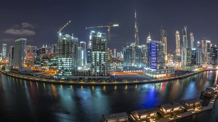 Night city with bright skyscrapers aerial timelapse near canal and Downtown towers in the background in Business Bay, Dubai, United Arab Emiratesの写真素材