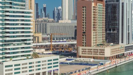 Construction between modern skyscrapers in Business bay aerial timelapse with huge machines and cranes on the coast of canal in luxury Dubai city, United Arab Emiratesの写真素材
