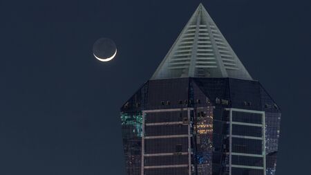 Nighttime view of Moon and lights from skyscrapers at evening aerial timelapse. Illuminated huge...