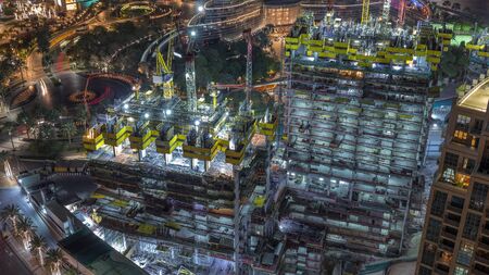 Aerial view of a skyscrapers under construction with huge cranes night timelapse in Dubai. Downtown district with fountains on a background. United Arab Emiratesの写真素材