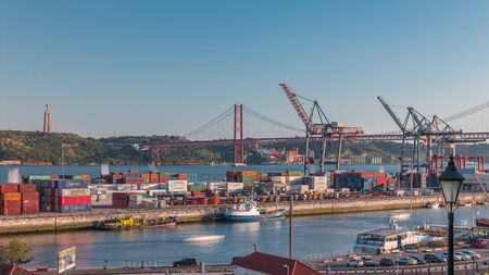 Skyline over Lisbon commercial port timelapse, 25th April Bridge, containers on pier with freight cranes, city train Lisbon, Portugal. Aerial view before sunsetの写真素材