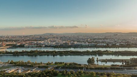Aerial panoramic view of Vienna city with highway intersection, historic buildings and a riverside promenade timelapse in Austria. Evening skyline before sunset from Danube Tower viewpointの写真素材