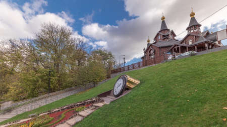 The temple in honor of the icon of the Mother of God Joy and Consolation and clock on flowerbed in Sarjin yar panoramic timelapse with playground in Kharkov, Ukraineの写真素材