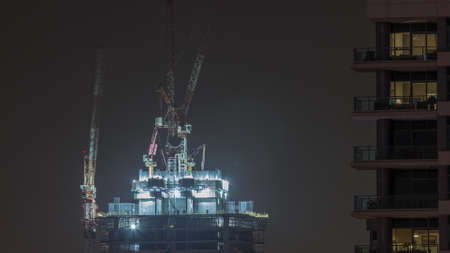 Skyscraper under construction with cranes and iron frame night timelapse