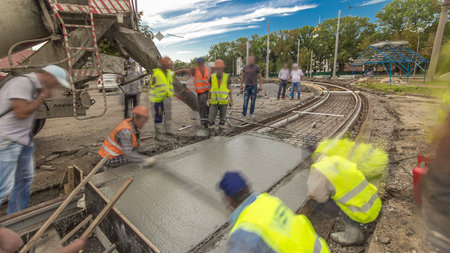 Concrete works and leveling for road construction with many workers and mixer timelapse hyperlapse. Pouring mortar to metal reinforcement. Reconstruction of tram tracksの写真素材