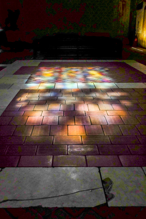 Sunlight projects colored light through stained glass windows onto the tiled floor of the church interior.のeditorial素材