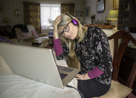 A mother at home,online with her computer displaying mixture of amusement and sadness at what she is seeing.の写真素材