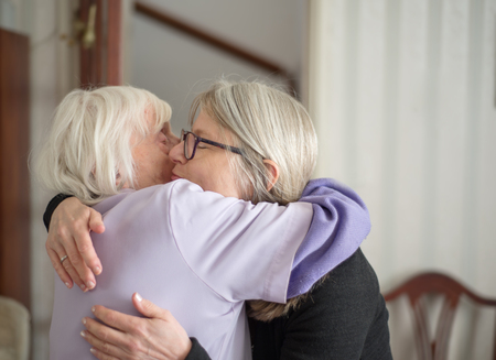 After a visit to see her elderly and sight impaired mother,the daughter hugs and says goodbye to her mom, before her long drive back home.の写真素材
