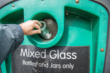 Putting glass bottles and jars into collection bin at local recycling center,Hampshire,UK.bottle bank.の写真素材