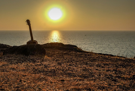 A baby acoustic guitar,leaning against rocks near the edge of the cliffs,near Gokarna beach,about to be played as the sun setsの写真素材