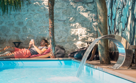 A young traveler relaxes in the shade by the pool at the Old Town Hostel,East wing on a hot sunny afternoon.のeditorial素材