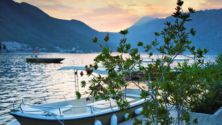 Beautiful evening dusk placid waters and setting sun behind distant mountains,boats and foliage in the foreground.の写真素材