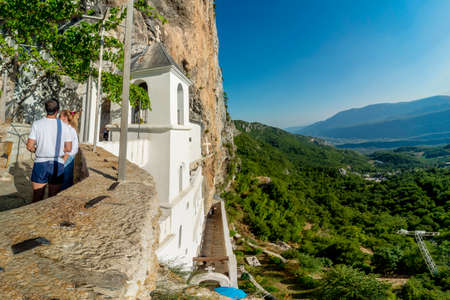 Ostrog,Montenegro-September 13 2019: Visitors to the monastery overlook the Zeta valley and Bjelopavlici plain,from a high balcony,on a sunny afternoon, at Montenegro's most popular pilgrimage site.のeditorial素材
