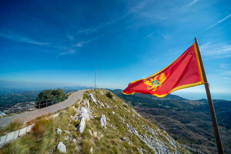 At the summit of Lovcen mountain,the majestic red national flag of the balkan state flapping in the wind,against clear,blue sunny skies of late summer.のeditorial素材