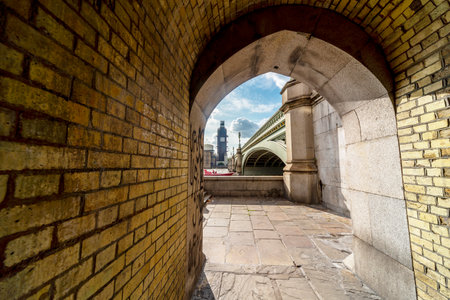 Looking across to Westminster Palace and Big Ben under renovation,summer sunlight shining into the brick tunnel that runs under the iconic bridge,crossing the River Thames.の写真素材