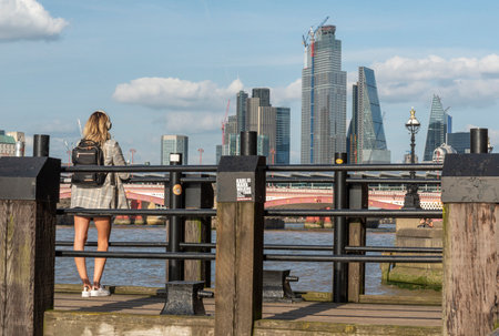 London,England,UK-July 21 2019: A young woman stands on the historic old wooden Gabriel's Pier,looking across the water at iconic modern buildings of the city skyline,on a warm,sunny late afternoon.のeditorial素材