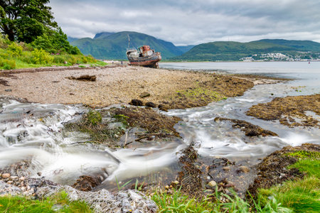 Water flows from a stream into the shore of Loch Linnhe,near to the stranded fishing vessel,across...