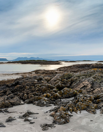 Beautiful remote,deserted beach with white sands,in mid summer,on the west coast of Scotland,at edge of Scottish Highlands,clear,calm sea,white cottages in the distance,at dusk,rugged rocks at low tide.の写真素材