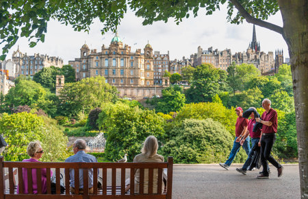 Edinburgh,Scotland-July 30 2022:Folks relax on a bench, while others stroll the park next to the Scott Memorial,against a backdrop of Georgian buildings and museum,on a warm sunny afternoon.のeditorial素材
