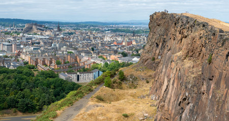 Edinburgh,Scotland-August 01 2022: Visitors climbing to the iconic summit,stand at the precipice of a giant vertical cliff,in awe of views across Edinburgh,on a summer day in Scotland's capital.のeditorial素材