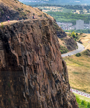 Edinburgh,Scotland-August 01 2022: Visitors climbing to Arthur's seat,stand at the precipice of a high vertical cliff in awe of views across Edinburgh City,on a summer day in Scotland's capital.のeditorial素材
